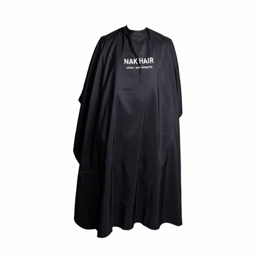A black salon cape with 'NAK HAIR' printed in white on the chest, displayed against a solid pale pink background.