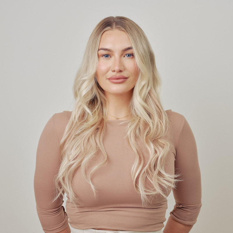 Woman with long blonde hair clip in hair extensions against a plain background