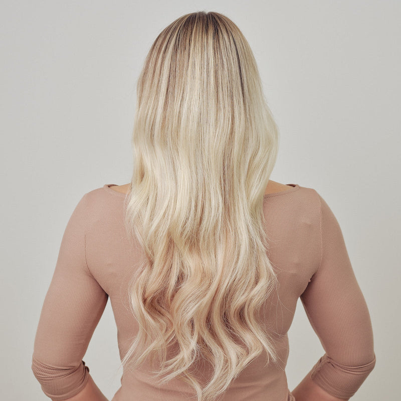 Person with long blonde hair wearing a sheer beige top against a plain background