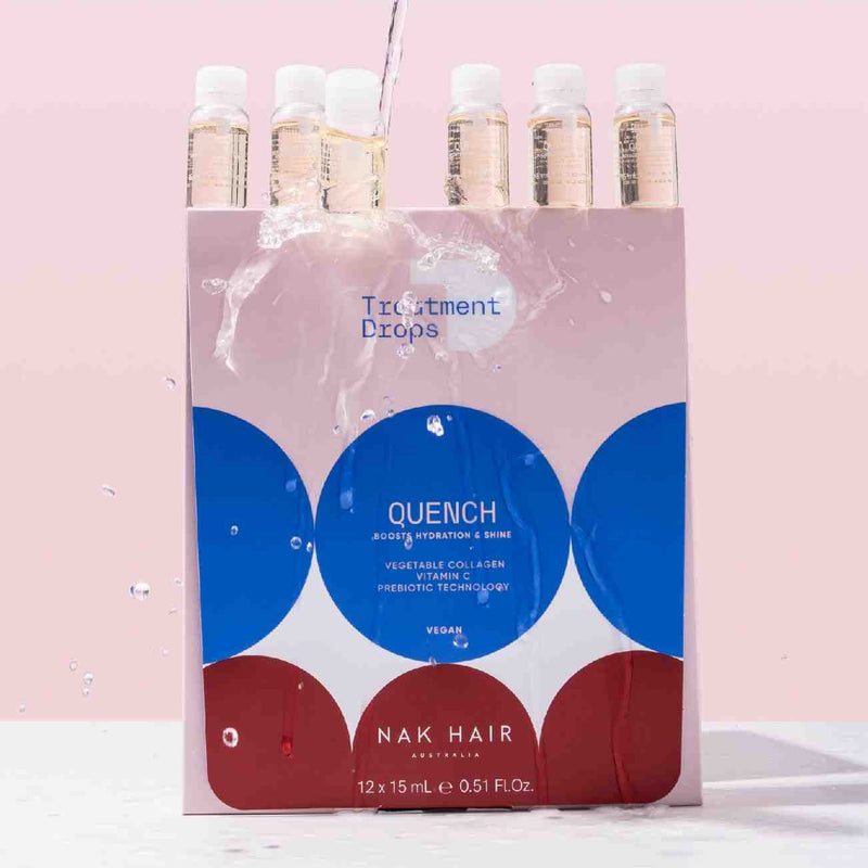 A pink, white, and blue box of NAK HAIR Quench Treatment Drops with water being poured over the top, showing the clear bottles and liquid splash against a solid pink background.