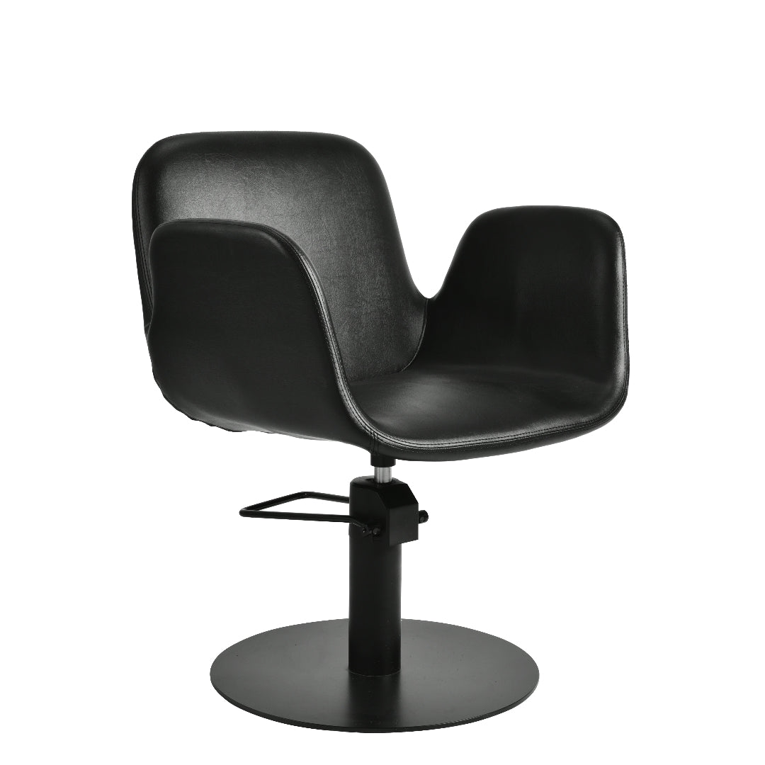A modern black salon chair with a curved, sculptural seat and backrest, mounted on a black hydraulic swivel base with a circular footrest, shown against a plain white background.